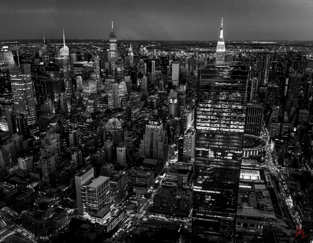 A black-and-white aerial view of Midtown Manhattan at night, with the NEW YORKER sign and the Empire State Building.